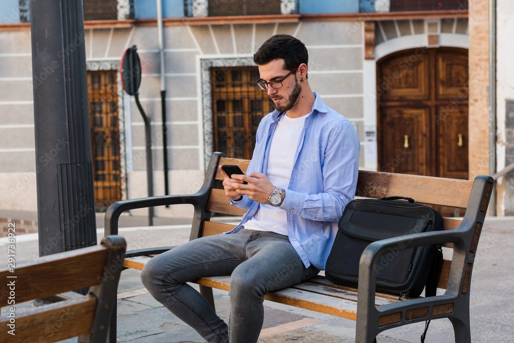 Young businessman is sitting on a bench while he is talking on the mobile