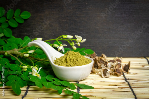 Moringa oleifera powder in white ceramic and green leaves on wooden background. Moringa products concept. 