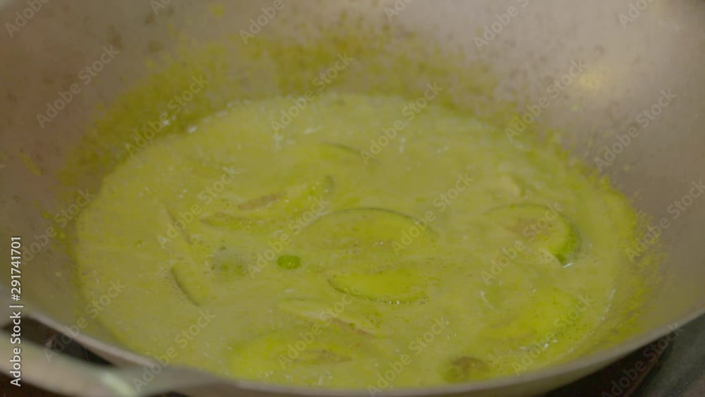 A daylight closeup shot of meat and cucumbers in boiling curry sauce being cooked in a large metal pan using a flat steel spoon. A daylight closeup shot of meat and cucumbers in boiling curry sauce being cooked in a large metal pan using a flat steel spoon.