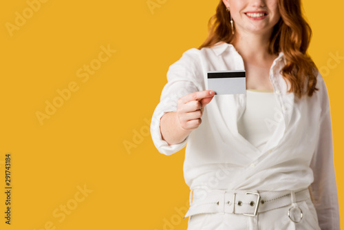 cropped view of cheerful redhead girl holding credit card isolated on orange