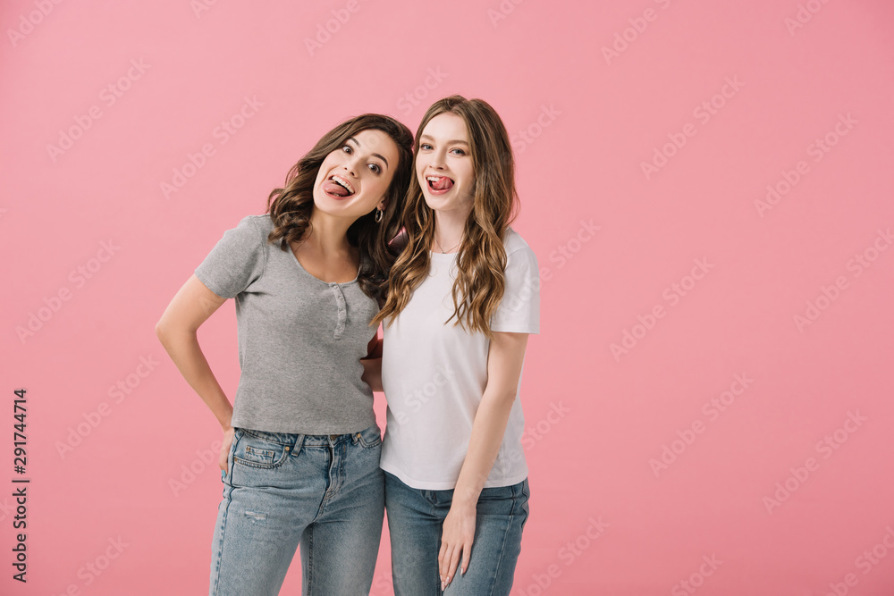 attractive and smiling women in t-shirts with sticking out tongues looking at camera isolated on pink attractive and smiling women in t-shirts with sticking out tongues looking at camera isolated on pink