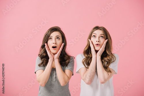 attractive and shocked women in t-shirts looking up isolated on pink