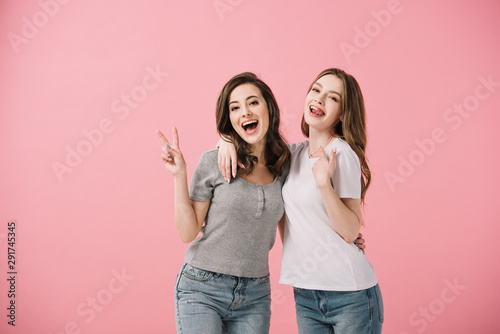 attractive and smiling women in t-shirts looking at camera and showing peace sign isolated on pink © LIGHTFIELD STUDIOS