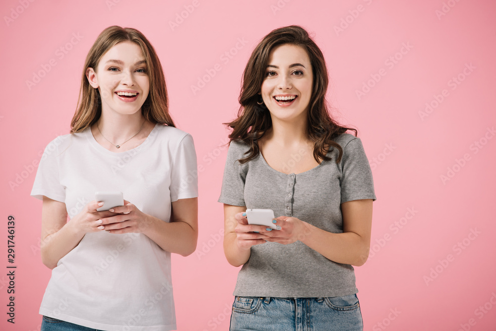 attractive and smiling women in t-shirts holding smartphone isolated on pink attractive and smiling women in t-shirts holding smartphone isolated on pink