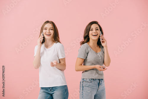attractive and smiling women in t-shirts talking on smartphones isolated on pink