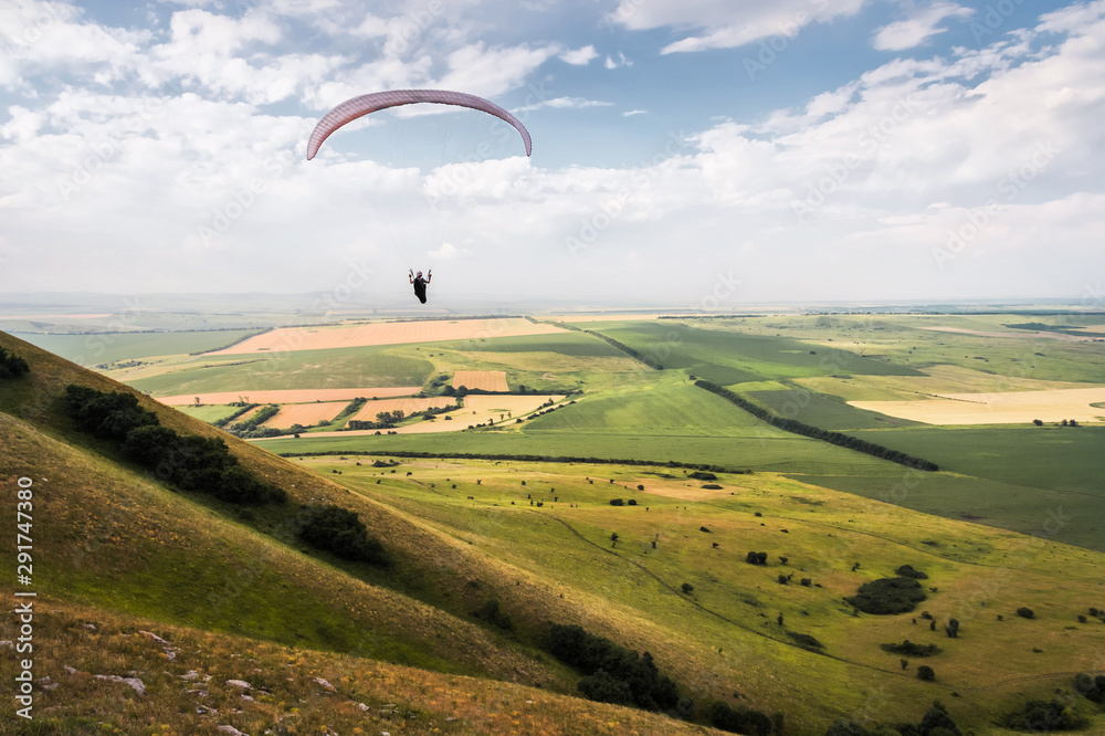 A white-orange paraglider flies over the mountainous terrain A white-orange paraglider flies over the mountainous terrain