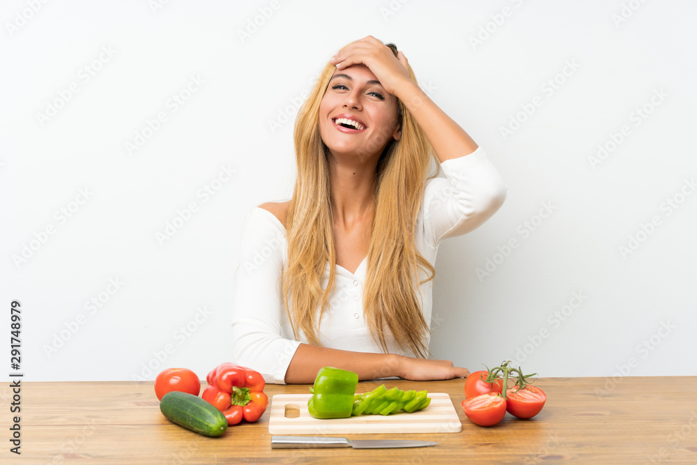 Young blonde woman with vegetables in a table laughing Young blonde woman with vegetables in a table laughing