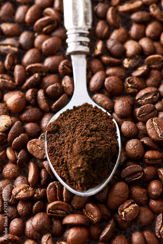 Ground coffee in a spoon viewed from above with coffee beans in background. Top view