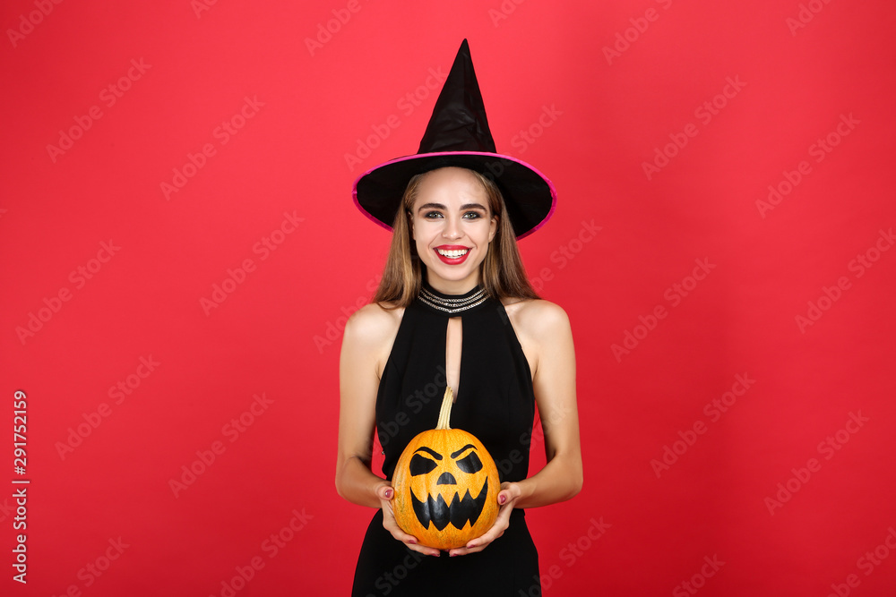 Beautiful woman in black costume holding halloween pumpkin on red background