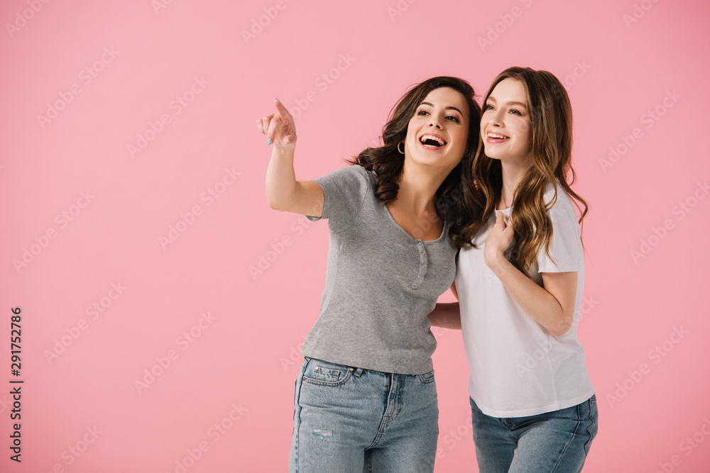 attractive and smiling women in t-shirts pointing with finger isolated on pink attractive and smiling women in t-shirts pointing with finger isolated on pink