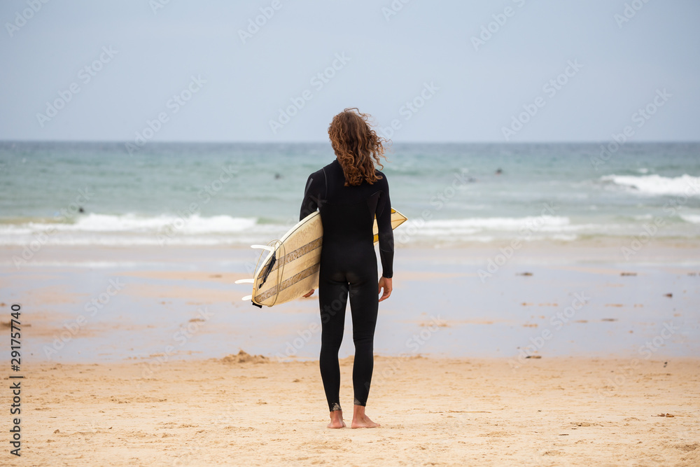 Young man in black wetsuit in the beach with surfboard on daytime Young man in black wetsuit in the beach with surfboard on daytime