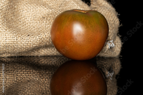 One whole fresh green red tomato with jute bag isolated on black glass