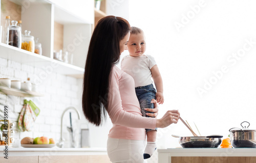 Young mother preparing dinner with little son, kitchen interior