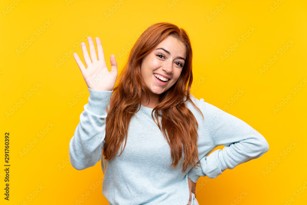 Teenager redhead girl over isolated yellow background saluting with hand with happy expression Teenager redhead girl over isolated yellow background saluting with hand with happy expression
