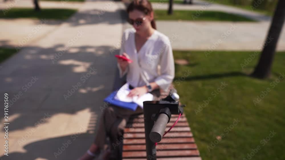 Female hipster with a smartphone in her hands makes a sale via the Internet, against the background of the steering wheel from an electric bike. Female hipster with a smartphone in her hands makes a sale via the Internet, against the background of the steering wheel from an electric bike.