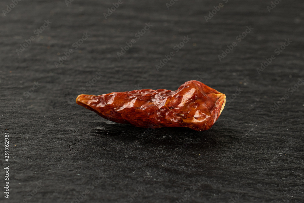 One whole dry red chili pepper peperoncino on grey stone One whole dry red chili pepper peperoncino on grey stone