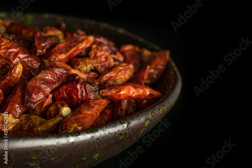 Lot of whole dry red chili pepper peperoncino closeup on grey ceramic plate isolated on black glass