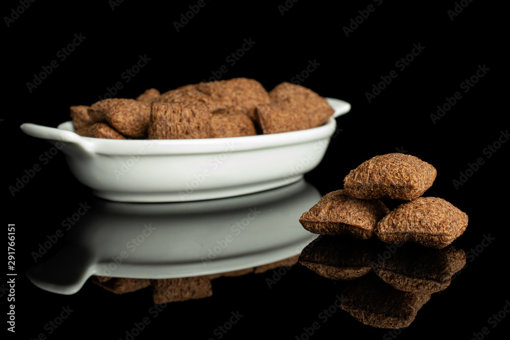 Lot of whole crispy brown cereal pillow in white oval ceramic bowl isolated on black glass Lot of whole crispy brown cereal pillow in white oval ceramic bowl isolated on black glass