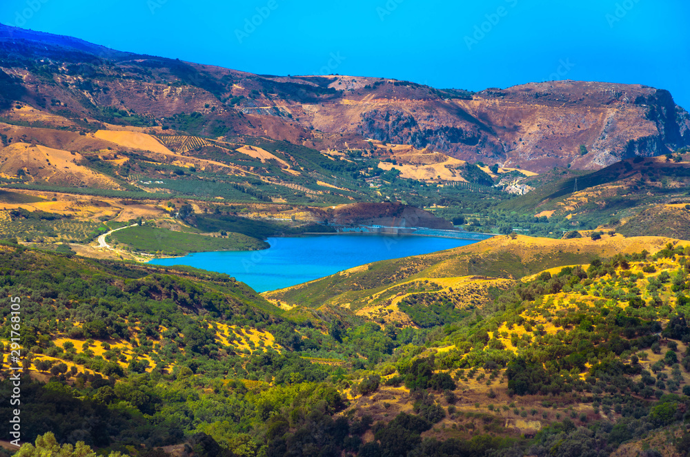 scenic view of cretan landscape at sunset.Typical for the region olive groves, olive fields, vineyard and narrow roads up to the hills. Potami dam lake in foreground.