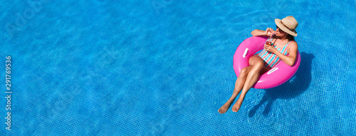 Young woman with sunglasses, hat and swimsuit in a blue pool. Pretty girl on a pink float enjoying the summer while having a cocktail.