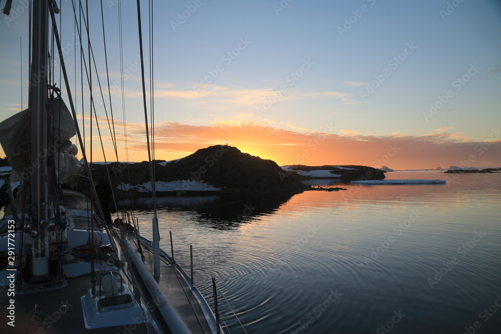 widok z jachtu na spokojne zimne wody oraz górzyste i ośnieżone wybrzeże antarktydyo zachodzie słońca