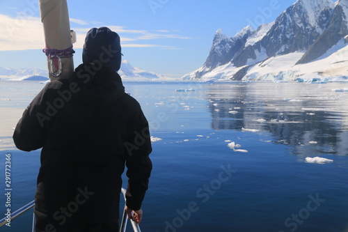 człowiek z tyłu stojący na jachcie i patrzący na piękne górzyste ośnieżone wybrzeże antarktydy