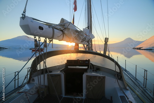 zachodzące słońce widziane z jachtu pomiędzy masztami na spokojnych wodach u wybrzeża antarktydy