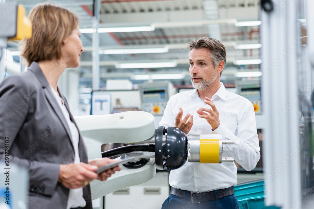 Businesswoman and man talking at assembly robot in a factory Businesswoman and man talking at assembly robot in a factory