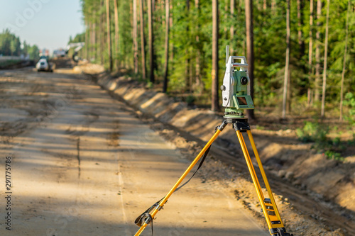 Surveyor engineer with equipment (theodolite or total positioning station) on the construction site of the road or building with construction machinery background