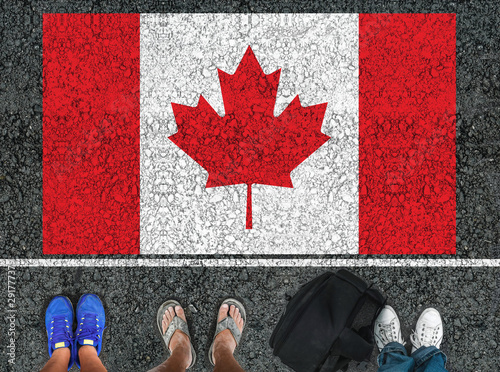 Fotografie people legs  is standing on asphalt road next to flag of Canada and border