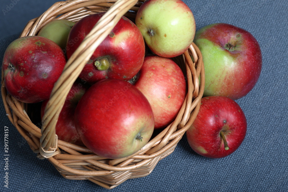 Wicker basket with ripe juicy apples. Nearby are a few apples. New crop. On a gray background. View from above. Wicker basket with ripe juicy apples. Nearby are a few apples. New crop. On a gray background. View from above.