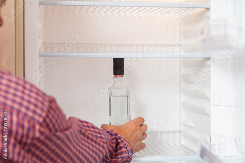 Hand takes bottle of vodka in empty fridge