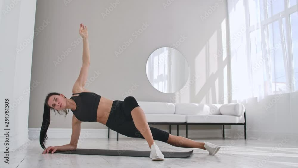 Young sexy brunette woman in sportswear doing side plank exercise with a tilt at home in a white interior. Slow motion. Young sexy brunette woman in sportswear doing side plank exercise with a tilt at home in a white interior. Slow motion.