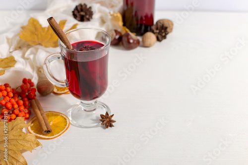 A cup of mulled wine with spices, bottle, scarf, spices, dry leaves and oranges on the table. Autumn mood, method to keep warm in cold, copy space.