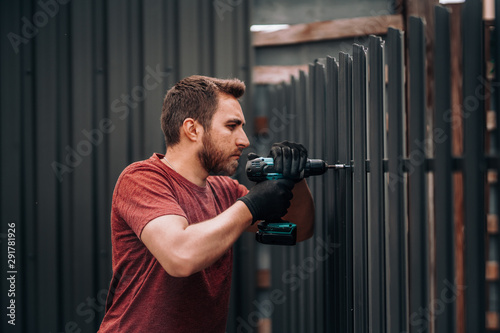 Worker using screwdriver and drilling screws into metal fence. Construction works