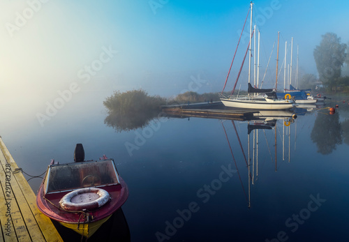 Autumnal mist on a river with sailboats and fishing boats anchored in harbor,...