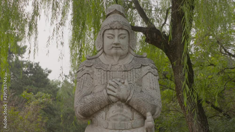 A daylight closeup shot of a Ming warrior sculpture ornamentation carved from stone and placed in a public park near the Ming Tombs. A daylight closeup shot of a Ming warrior sculpture ornamentation carved from stone and placed in a public park near the Ming Tombs.