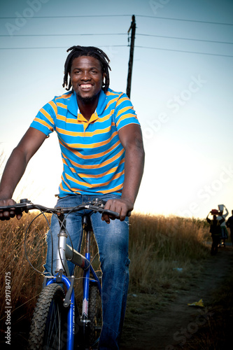 Young black adult male rides a bicycle through the streets while smiling at camera