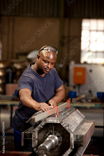 Factory worker attaching charged magnets to industrial magnet in magnet factory, Gauteng, South Africa