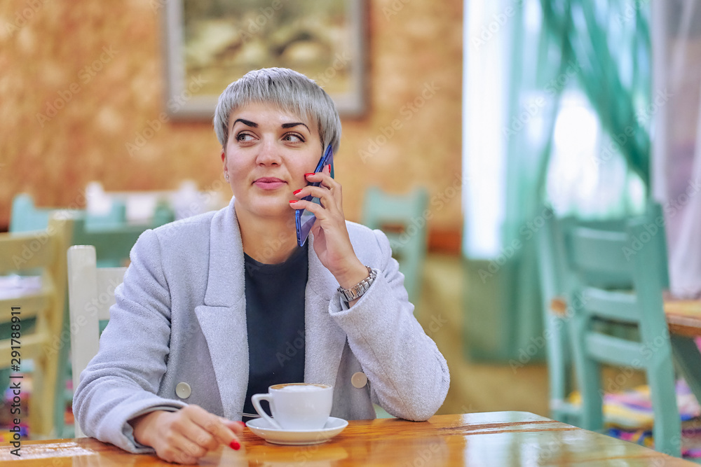 short-haired business woman in a light coat in the morning in a cafe takes a call short-haired business woman in a light coat in the morning in a cafe takes a call