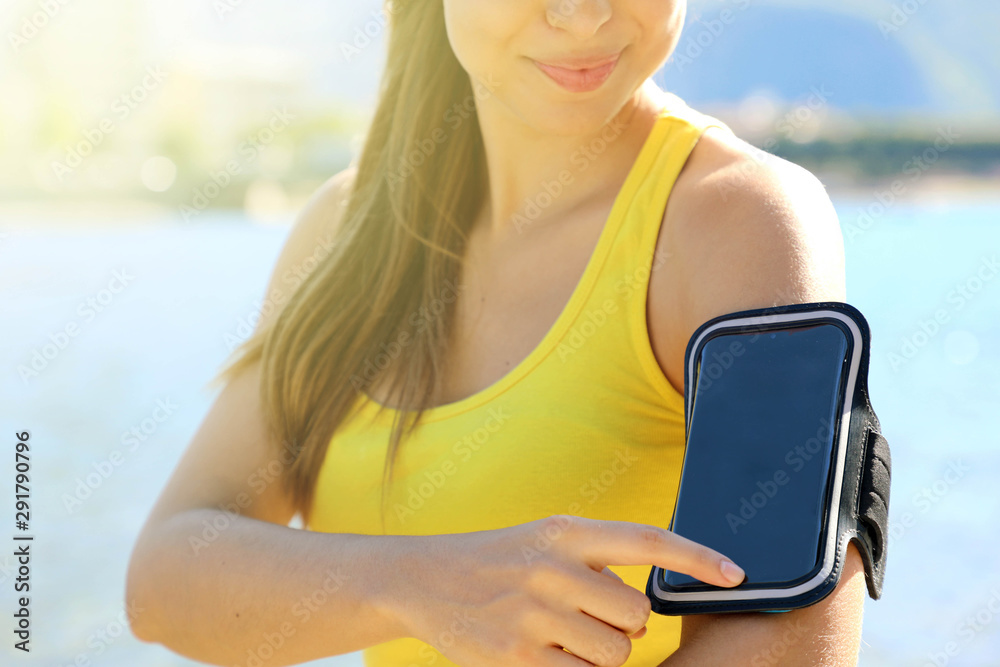 Sport armband for smartphone. Sporty woman touching her smart phone before outdoor fitness workout at the beach.