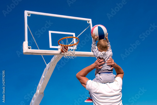 Back view of senior man teaching little boy to play basketball