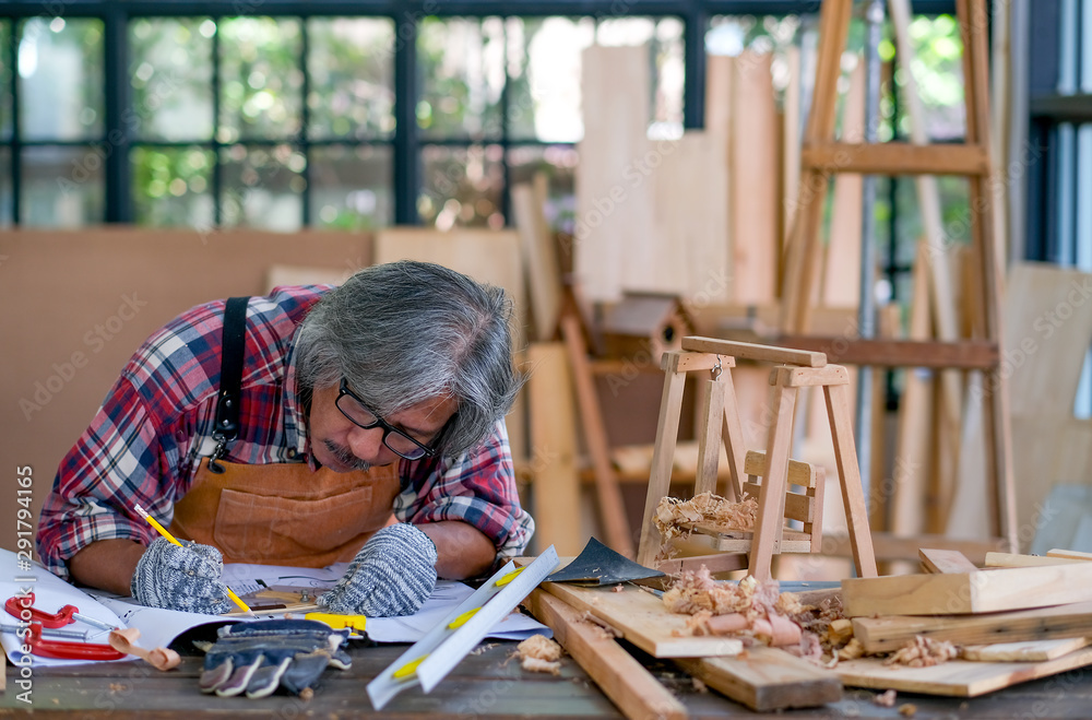 Fotka „Old Asian craftsman act as write something on the paper in the room  with wood pile and surround with glasses. Concept of using natural material  to produce hand-made woodworking after retire.“ ze