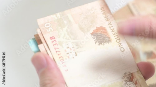 Fingers sliding Brazilian banknotes and throwing them on the desk. Squandering money. Real BRL money bills.