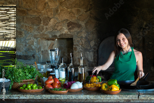 girl on a .girl cooking in rustic kitchen holding a wooden spoon and a noodle picker.
