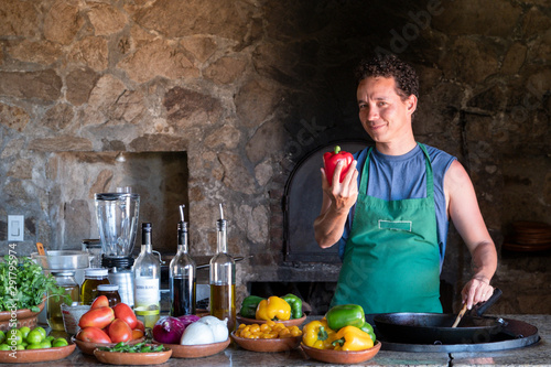 man cooking and holding a red pepper in a rustic kitchen