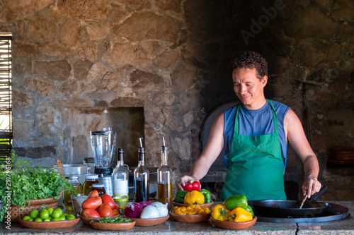man cooking and holding a red pepper in a rustic kitchen