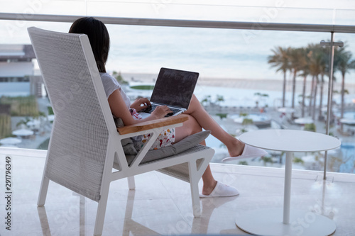 girl sitting in front of a beach view with a laptop on the lap