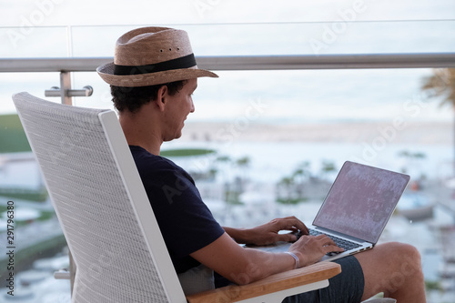 man sitting with a laptop on his lap writing, in front a beach view