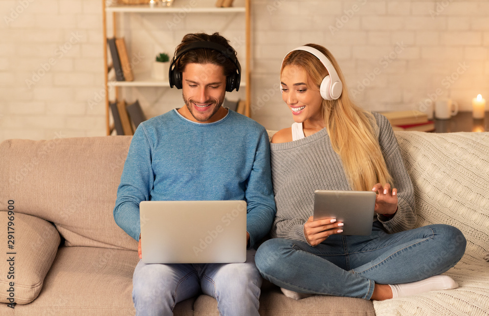 Couple Using Laptop And Tablet Sitting On Couch At Home